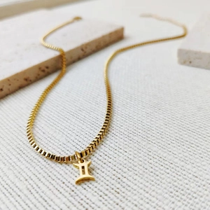 Close-up of golden Gemini zodiac symbol pendant on a classic steel box chain necklace