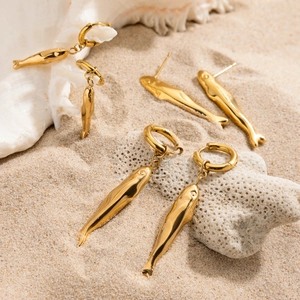 Detailed view of three pairs of gold fish earrings on sand with shells and coral stones