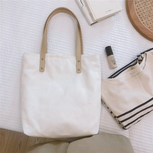 Detail of white canvas tote bag with reinforced faux leather handles and metal rivets