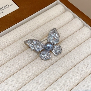 Macro shot of silver butterfly brooch featuring a grey-blue pearl and zircon pavé wings