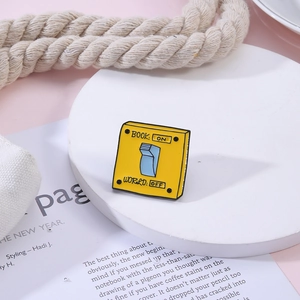 Enamel pin featuring a yellow wall switch design with BOOK ON and WORLD OFF text