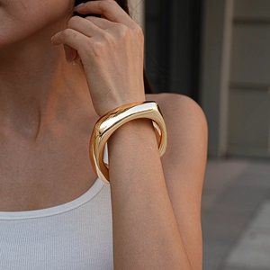 Close-up of a high-polished golden chunky square bracelet on a model wearing white