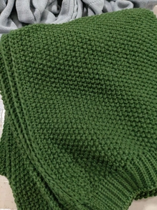 Close-up detail of green chunky knit blanket showing texture and tassel craftsmanship