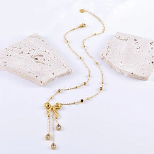 Golden bow necklace with teardrop crystal pendants on white stone background decor