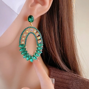 Close-up of a model wearing an oval green rhinestone earring with gold metal finish
