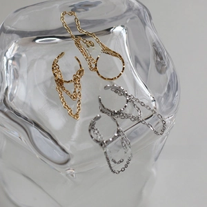 Detail view of gold and silver tassel chain ear cuffs on reflective glass background