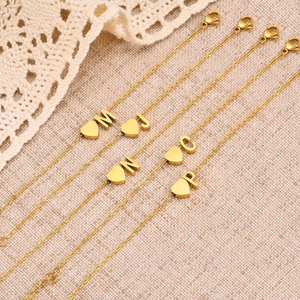 Detail of gold heart charms with engraved letters on delicate stainless steel chains