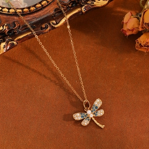 Nahaufnahme des goldenen Libellenanhängers mit blauen Kristallen und Perlenkette