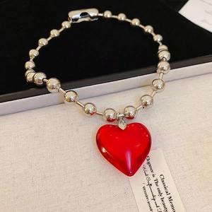 Macro shot of silver beaded chain with a translucent red heart pendant on soft texture