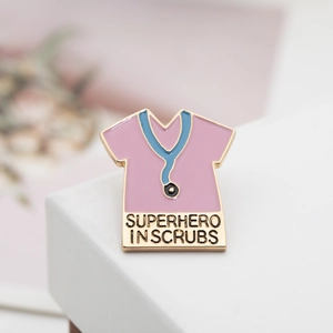 Detailed close-up of a pink scrub top enamel pin with a blue stethoscope and slogan