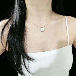 Dettaglio di una collana dorata con ciondolo quadrato bianco e motivo a cuore dorato
