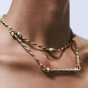 Detail of colorful braided cord necklace with gold cylinder pendant and pearl accents
