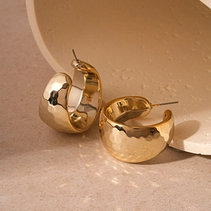 Macro detail of gold C-shaped wide hoop earrings with hammered textured metal surface