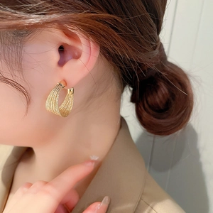 Detailed close-up of a model wearing gold woven texture hoop earrings with elegant styling