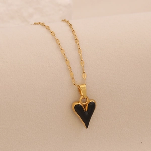 Gros plan sur la chaîne dorée et le pendentif cœur noir brillant sur fond beige doux