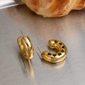 Detailed view of chunky gold heart-cutout C-shaped hoop earrings on a metal tray.