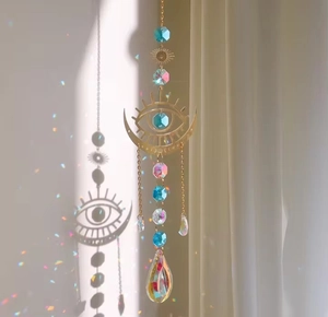 Detail of crystal suncatcher with moon and eye motifs reflecting rainbow light on a wall