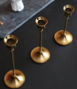 Detail van drie koperen kandelaars met geborsteld gouden afwerking op donkere achtergrond