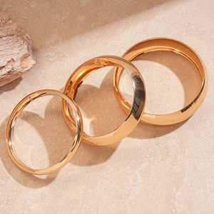 Detailed view of three polished gold metal bangles in varying widths on a stone surface