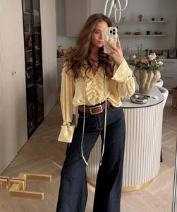Detail of light yellow ruffled blouse paired with dark blue wide leg jeans and brown belt