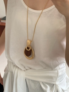 Detail view of long necklace featuring gold matte ring and dark wood circular pendant