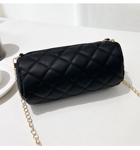 Close-up of black quilted cylinder bag with gold chain strap on a white surface