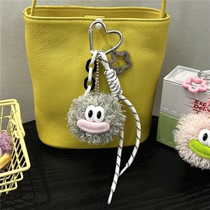 Close-up of a grey plush monster keychain with a heart-shaped clasp on a yellow bag