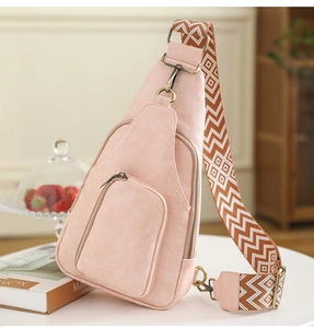 Pink PU leather crossbody bag detail with patterned wide fabric strap on a table