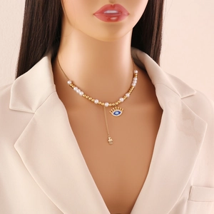 Golden pearl necklace with Hamsa hand and crown eye pendant worn by a model