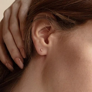 Close-up of minimalist gold star stud earring with a central diamond on model ear