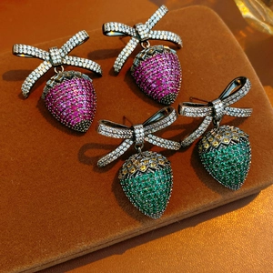 Macro detail of vintage bow strawberry earrings with pavé crystals on velvet