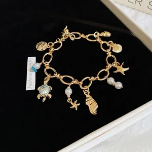 Golden ocean theme bracelet with sea turtle and pearl charms on black velvet background