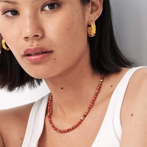 Detail of red beaded necklace and gold textured C-shape earrings on female model