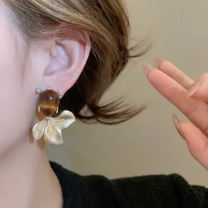 Elegant gold fish scale earrings with brown teardrop cat-eye stone on a female model