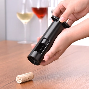 Electric wine bottle opener in black plastic held by hand over a wooden tabletop