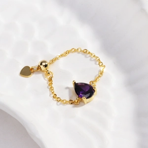 Détail d'une bague chaîne en or 18k avec pierre poire violette et breloque en cœur