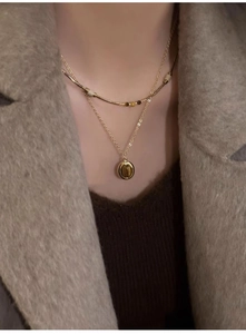 Close-up of layered gold necklaces with brown tiger eye pendant on a knit sweater
