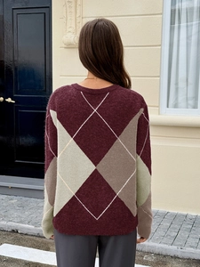 Détail macro du motif à losanges rétro sur un pull en maille bordeaux et vert foncé