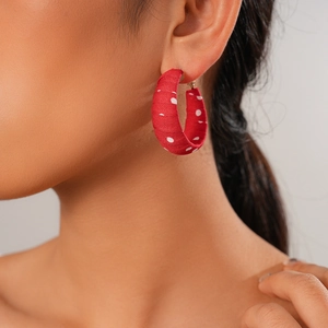 Detail of red fabric hoop earring with white polka dots on a soft aesthetic background