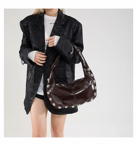 Detail of burgundy glossy patent leather underarm bag with silver stud accents on model