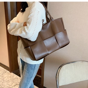 Brown woven leather tote bag shown on model with casual white sweater and jeans