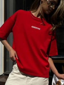 Dettaglio della T-shirt in cotone rosso con scritta ASSERTIVE e luce naturale esterna