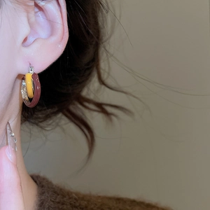 Detail of three interlocking circular hoop earrings in yellow, brown, and silver on model