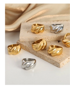 Close-up of twisted gold and silver croissant rings on beige stone and silk fabric