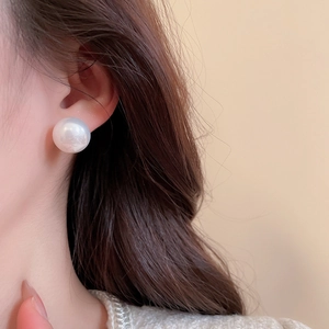 Close-up of model wearing large round pearl stud earring with silver needle