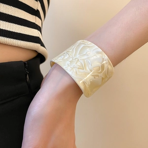 Close-up of wide acrylic open bangle with cream marble texture on a model's wrist
