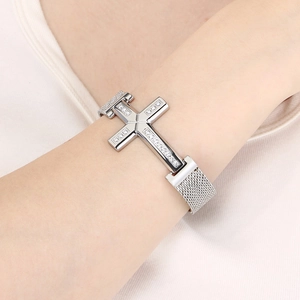 Close-up of a silver cross charm bracelet with rhinestones on a mesh watch strap