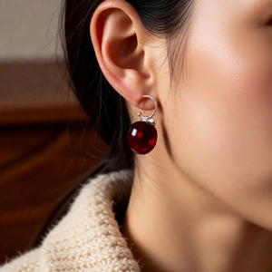 Close-up of a deep red cherry pendant earring on a model with knit sweater