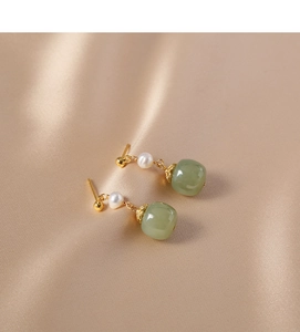 Macro detail of vintage gold pearl earrings with green jade on champagne silk fabric