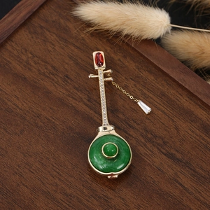 Chinese lute brooch with green jade ring and red stone on dark wood display
